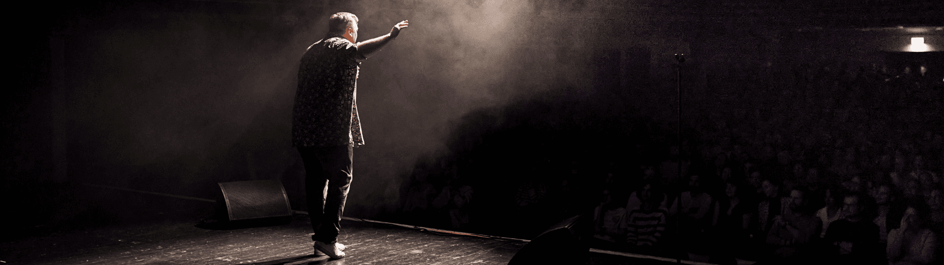 Benjamin on a dark stage with his arm raised toward the audience